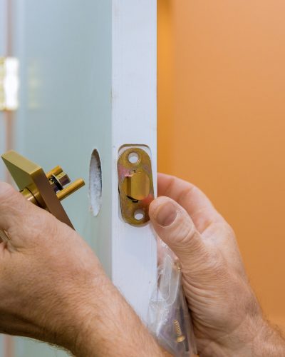Builder in installing a door lock the door of a new house hand close-up.